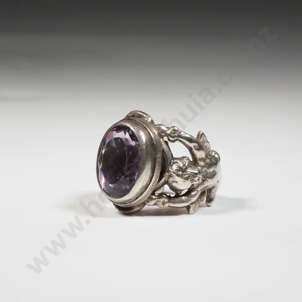 Sterling Silver Ring Set With An Amethyst Coloured Stone In An Ornate Frame With Cupids Image 1++